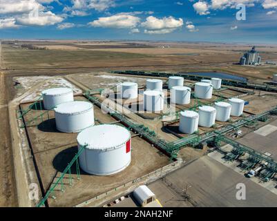 Aerial view of large round metal oil storage tanks with pipelines connecting them with blue sky and clouds, West of Carseland, Alberta Stock Photo