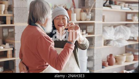 Pottery, creative and senior couple talking about art dancing together in a studio class. Elderly Asian man and woman hugging with love while learning Stock Photo
