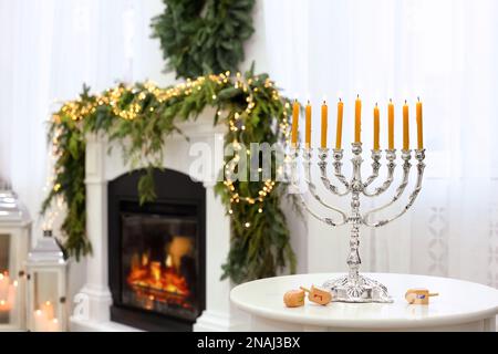 Silver menorah near dreidels with symbols He, Pe, Nun, Gimel on white table in room, space for text Stock Photo