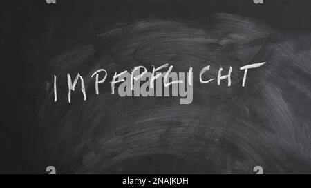 Impfpflicht translates as compulsory or mandatory vaccination in German language - text written in chalk on blackboard Stock Photo