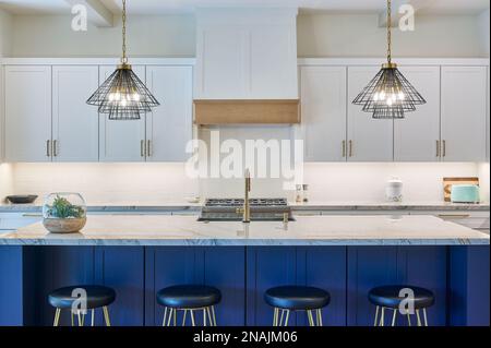 Straight on view of a contemporary kitchen with bar stools, pendant lighting, and cabinetry Stock Photo