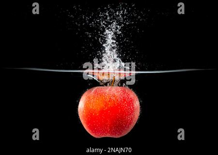red apple falling into splashing water Stock Photo
