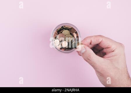 above view of hand putting coin in jar filled with small change Stock Photo
