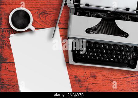 directly above view of old typewriter, cup of steaming hot coffee and stack of blank writing paper on red wooden desk Stock Photo