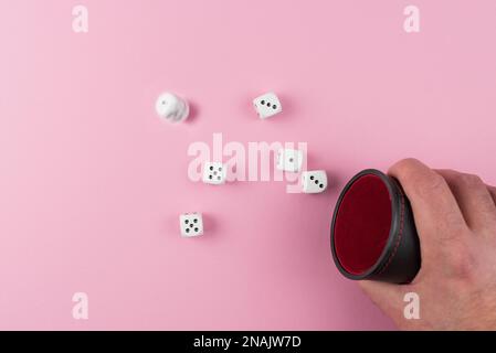 directly above view of player throwing or rolling dice using a dice shaker against pink background Stock Photo