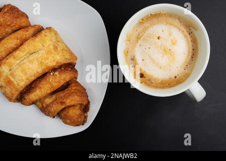 directly above view of Franzbrotchen pastry and cup of coffee on dark table, Franzbroetchen are a sweet cinnamon pastry and a local delicacy in and Stock Photo