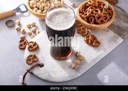 Dark stout beer in a tall glass, beer and snacks on the table Stock Photo