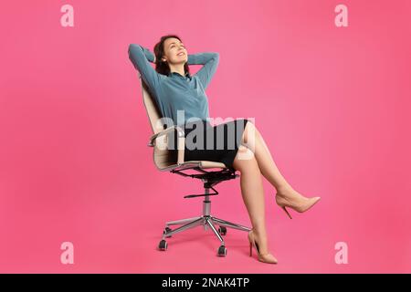 Mature businesswoman relaxing in comfortable office chair on pink background Stock Photo