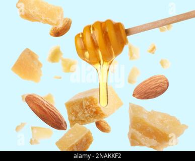 Pieces of delicious parmesan, almonds and honey falling on light blue background Stock Photo
