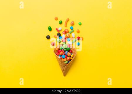 waffle cone full of assorted traditional candies falling out on colored background with copy space. Happy Holidays sale concept. Stock Photo