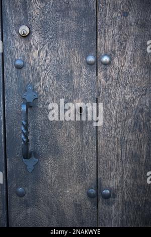 Old and modern lock on old dark door with iron handle in vertical Stock Photo
