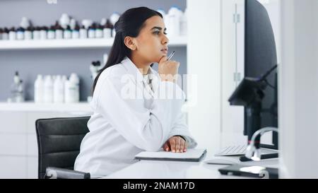 Young scientist using a computer and microscope in a lab. Female pathologist analyzing medical samples while doing experiments to develop a cure Stock Photo