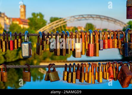 Love locks on wire cable romantic ritual in front of Luitpold bridge and Church of the Redeemer during sunset in Bamberg Germany Stock Photo