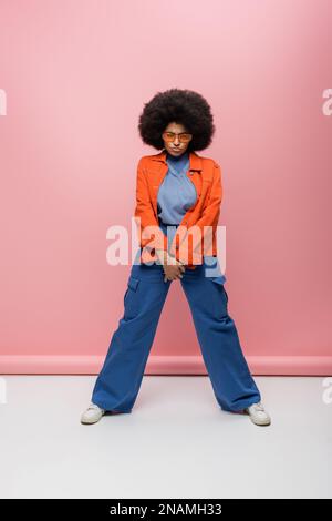 Full length of serious african american model in sunglasses standing on pink background,stock image Stock Photo