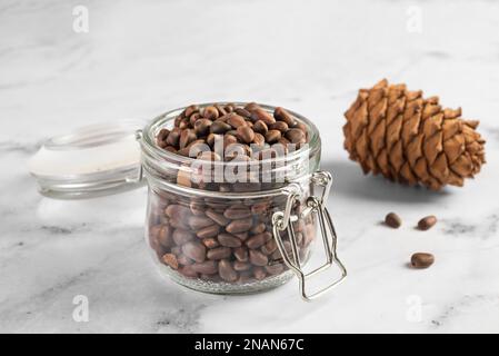 Pine nuts in a jar and a pine cone in the kitchen on a light background. The concept of organic food and protein food Stock Photo
