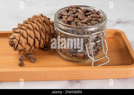 Pine nuts in a jar and a pine cone in the kitchen on a light background. The concept of organic food and protein food Stock Photo