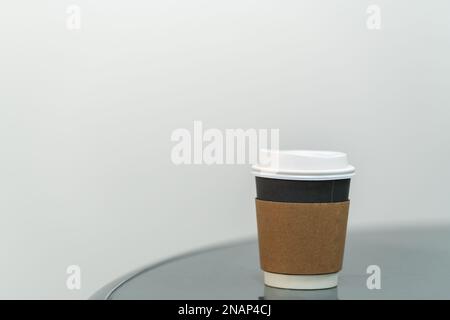 Closeup of takeaway paper cup with sleeve of hot coffee on round table with copy space. Stock Photo