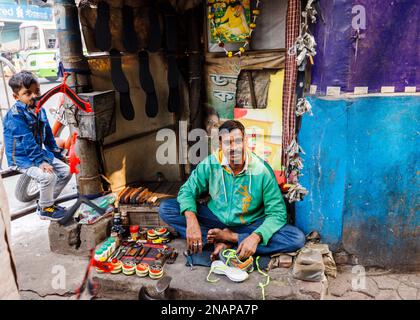 Local mender repairing shoes and shoe-shine at a small roadside pavement stall in Fariapukur, Shyam Bazar, Kolkata, West Bengal, India Stock Photo