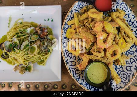 Mixed fried fish & seafood served. Top-up of two dishes with cooked pasta with clamshell & panned shrimps, small fishes, zucchini & calamari rolls. Stock Photo