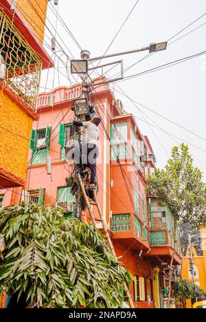 A local man working on electric lights and telephone wires at height up a ladder in Fariapukur, Shyam Bazar, a suburb of Kolkata, West Bengal, India Stock Photo