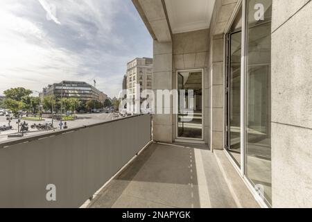 Terrace of an office with a gray granite facade with large doors and windows of white aluminum and glass and views of a square with little traffic Stock Photo