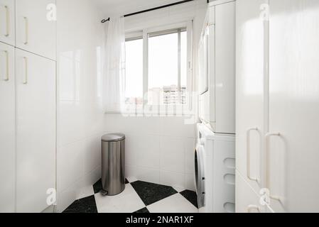 Zona de lavado y secado de ropa en una cocina amueblada con armarios blancos junto a una ventana Stock Photo