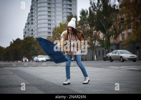 Woman with blue umbrella caught in gust of wind on street Stock Photo