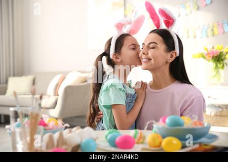 Happy mother with her cute daughter painting Easter eggs at table indoors Stock Photo