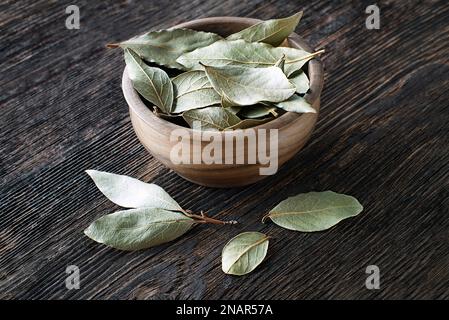 Dried bay leaves in bowl cleseup on wooden table background. Aromatic leaf used in cooking Stock Photo