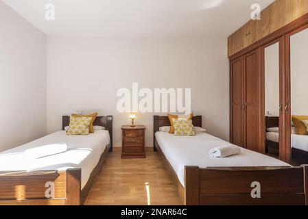 A bedroom with matching wooden single beds with a built-in wardrobe with central mirror doors Stock Photo