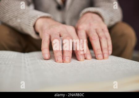 Close-up of visually impaired senior man using his hands to read book in Braille at table Stock Photo