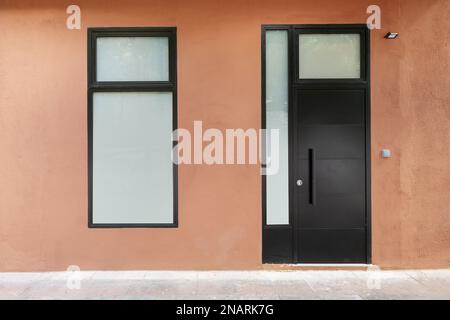 Exterior door of a house at street level with opaque glass windows on an earth-colored wall Stock Photo