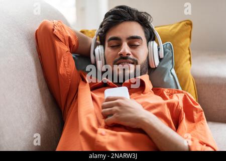 Relaxed guy resting on sofa at home, listening to music Stock Photo