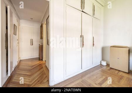 Hallway of a house with white painted walls, many built-in cabinets with wooden doors and brass handles Stock Photo