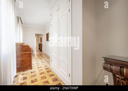 Corridor of a house with a beautiful wooden parquet floor in various shades and built-in wardrobes with white lacquered wooden doors Stock Photo