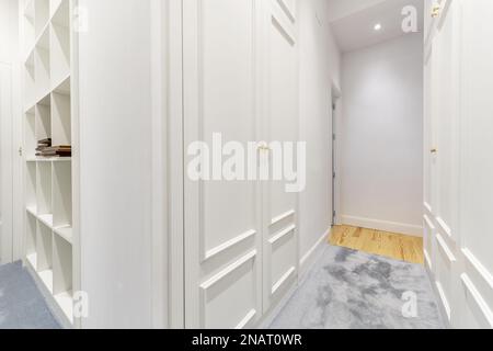 Walk-in wardrobe with blue carpeted floors, white lacquered doors and many shelves Stock Photo