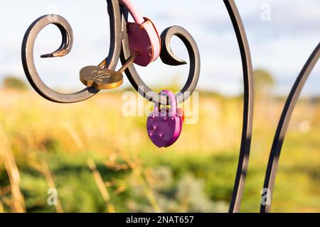Pink heart shaped lock hangs from bridge chain, wedding custom is symbol of eternal love, copy space Stock Photo