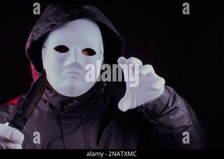 Masked person with black hooded jacket on and holding a knife in a threatening manner. Stock Photo