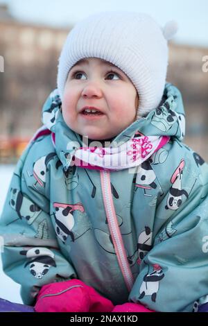 Girl with frozen red cheeks, in a hat, scarf, mittens and warm overalls Stock Photo
