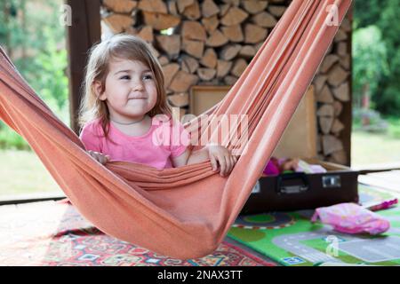 Happy Caucasian girl swinging on hammock in wooden veranda. Stock Photo