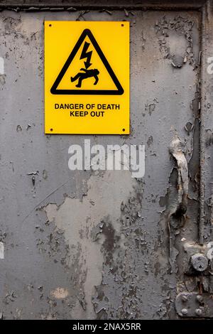 Electrical hazard warning notice reading Danger of Death Keep Out on an old corroded metal door with flaking grey paint. Stock Photo