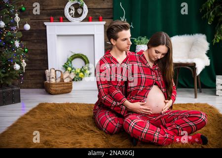 A couple dressed in identical checkered pajamas sit on the carpet. Stock Photo
