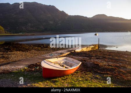 Small red rowboat, beached on the shores of Loch Duich, Scotland, in the late afternoon Stock Photo