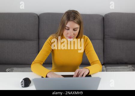 Beautiful blonde woman working on modern laptop computer. Young adult female person typing text on notebook pc at home Stock Photo