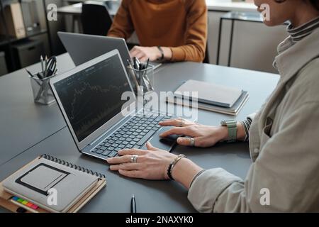 Close-up of young female broker with laptop analyzing financial data and drawing graph illustrating development of stock market Stock Photo