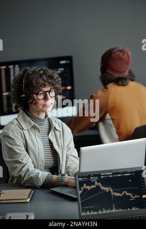 Young serious female operator of call center sitting by desk in front of laptop, working with online data and consulting clients Stock Photo