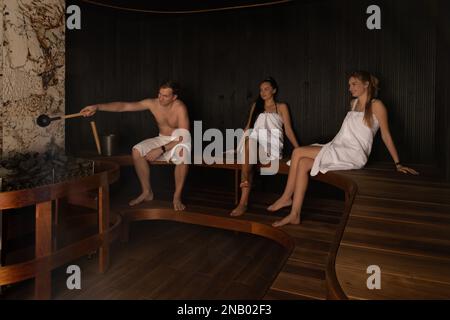 Three people in white spa towels relaxing in the finnish sauna steam room in the spa Stock Photo