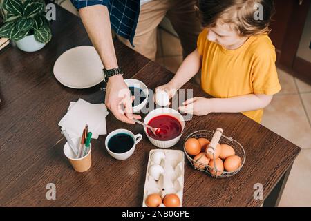 Easter day. Male Father and son painting eggs on wooden background. Family sitting in a kitchen. Preparing for Easter, creative homemade decoration Stock Photo