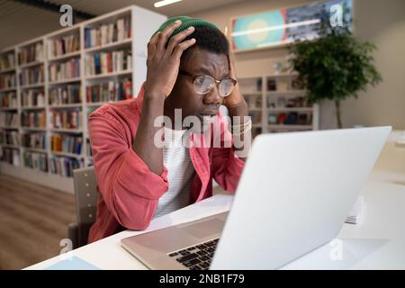 Unhappy black guy freelancer or student look at laptop screen shocked by error operational problems. Stock Photo