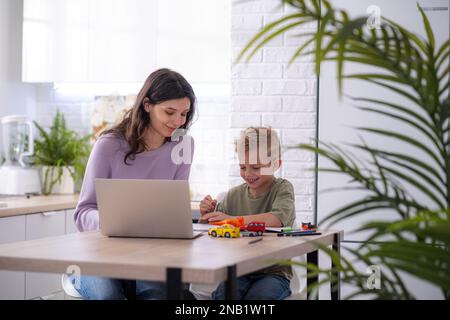 Work from home and family education, Mom and son using remote access technology for learning and work, woman works on laptop, child writes in textbook Stock Photo